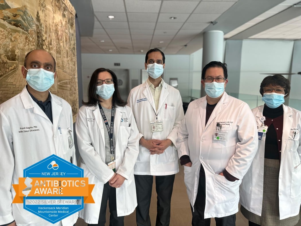 5 doctors in lab coats and face masks pose for a picture