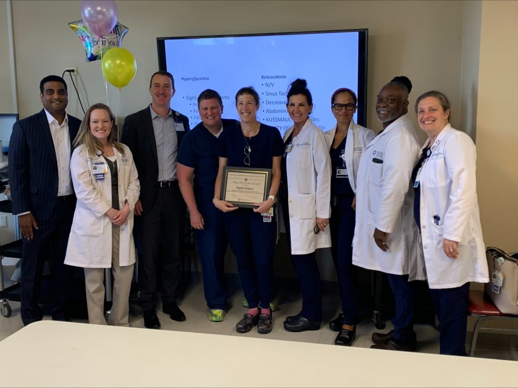 Meghan Hodgson holding her care award surrounded by her colleagues